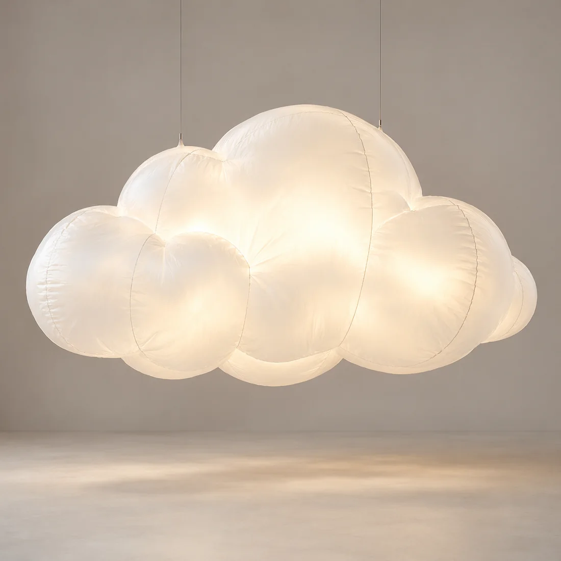 A warm white glowing inflatable cloud suspended by two thin wires against a neutral background.