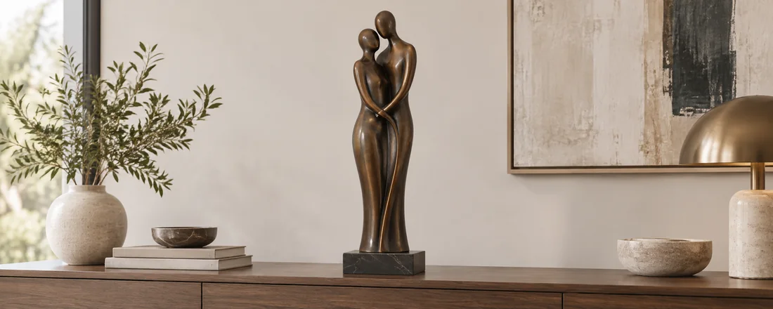 Two elongated abstract bronze coloured figures connected in an embrace on a small stone base.